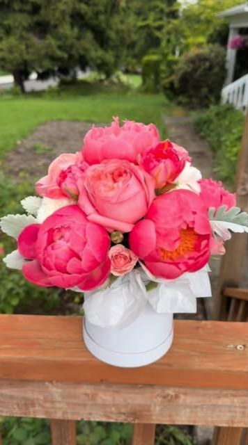 A coral peony arrangement sitting on the wooden flower bench in the front yard